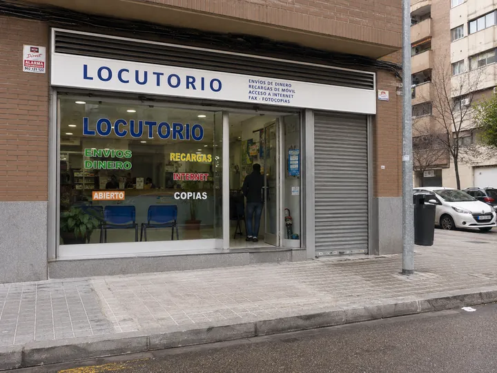Locutorio en una calle con naranjos y una moto aparcada