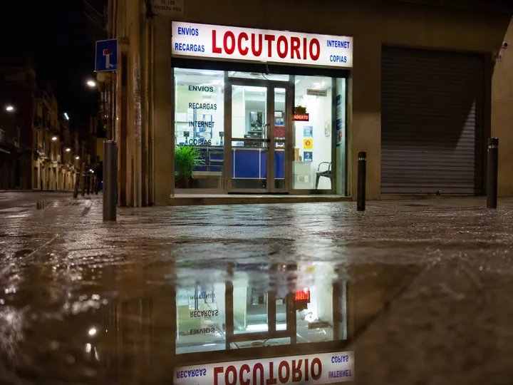 Rótulo de locutorio reflejado en un charco por la noche
